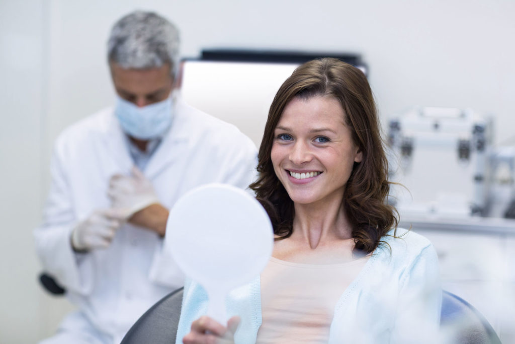 Woman holding mirror smiling when she see her porcelain veneers for the first time.