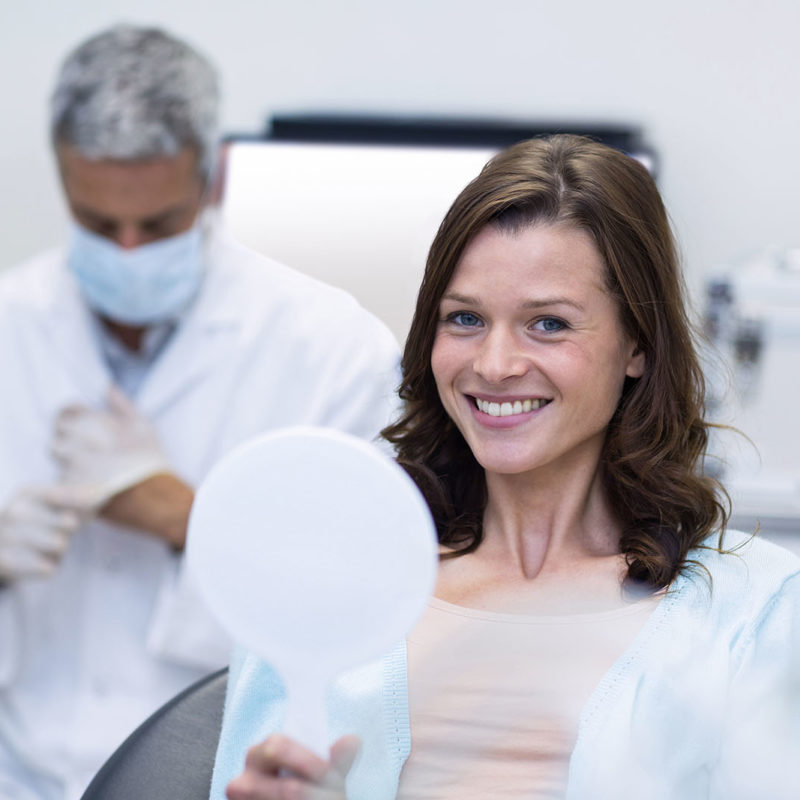 Woman holding mirror smiling when she see her porcelain veneers for the first time.