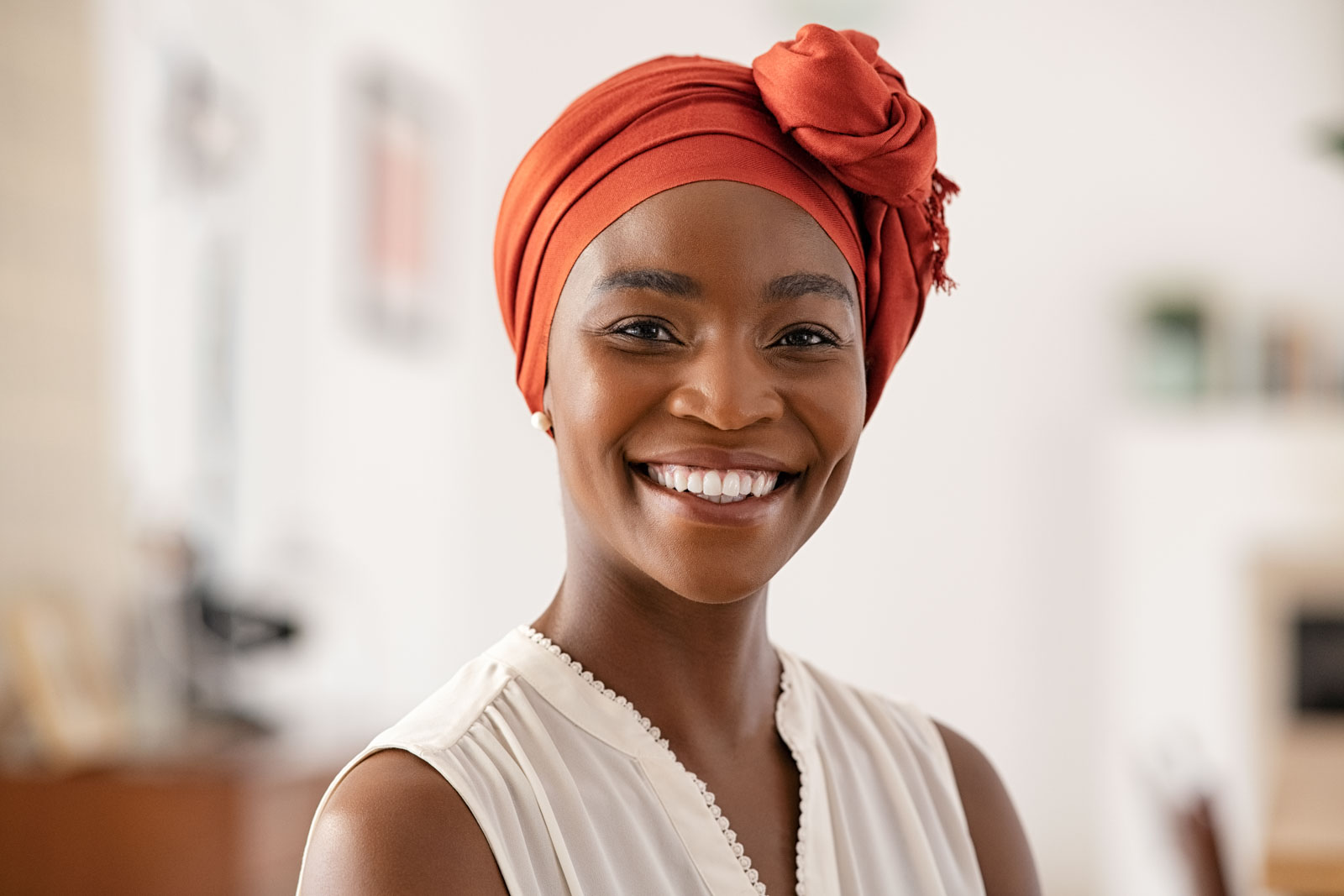 Smiling middle aged African american woman with headscarf at home. Cheerful mid adult black woman with turban looking at camera at home. Happy mid mature lady wearing traditional african scarf on head.