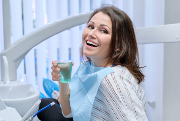 Happy mid adult woman patient in dental chair with glass of water, smile with healthy white teeth. Dental treatment, medicine dentistry and health care concept
