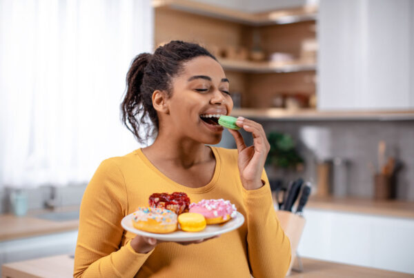 Glad millennial pregnant african american woman hold plate of sweets and eating cookies in minimalist kitchen interior, close up.