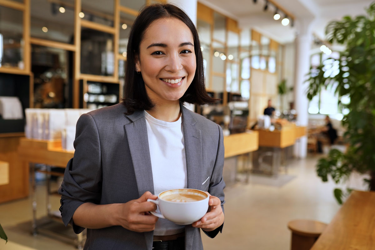 Smiling professional woman holding a latte in a Philadelphia cafe, highlighting the importance of dental health for coffee drinkers in Center City.