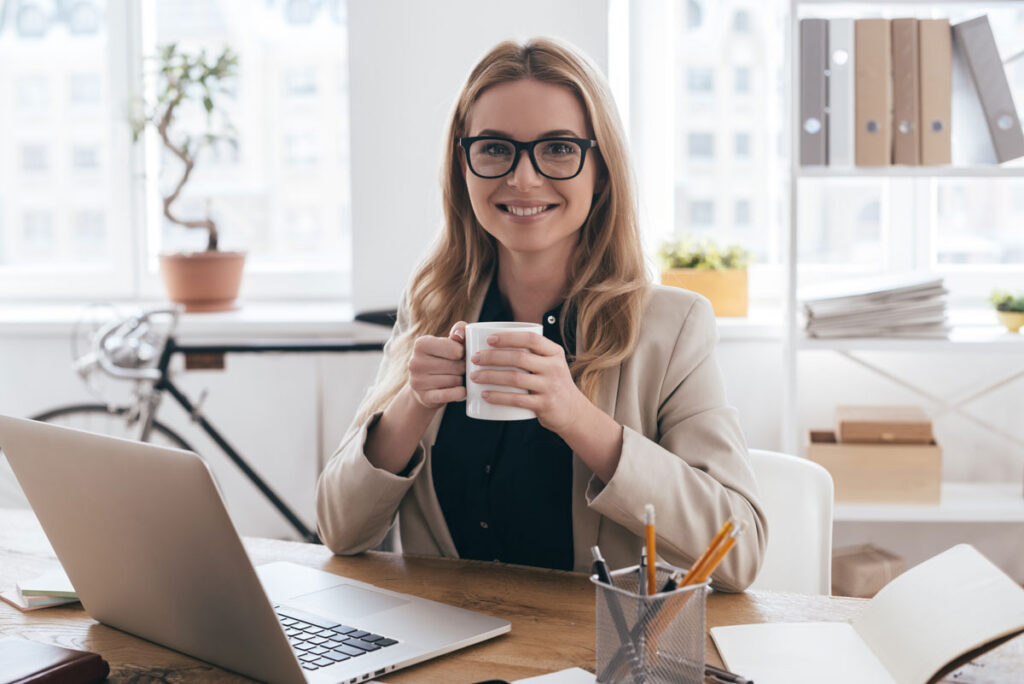 Professional woman with glasses holding a coffee mug at her desk, symbolizing the need for enamel protection for office workers in Center City Philadelphia.