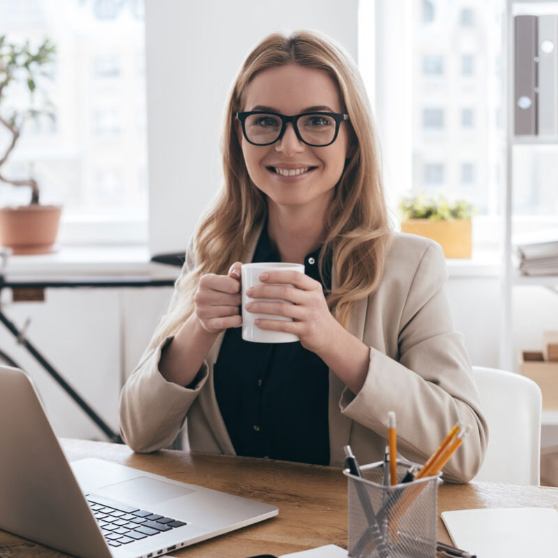 Professional woman with glasses holding a coffee mug at her desk, symbolizing the need for enamel protection for office workers in Center City Philadelphia.