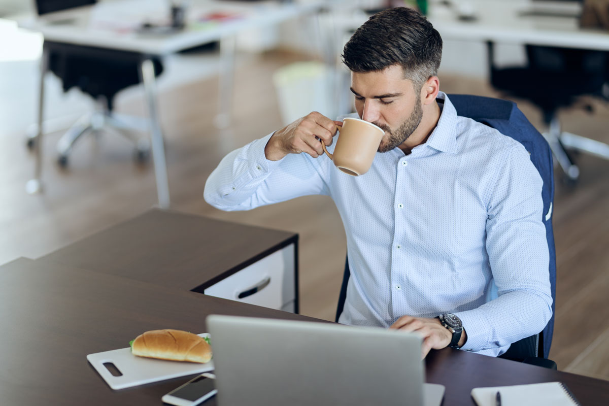 Professional man drinking coffee while working at a laptop in a Center City Philadelphia office, illustrating the risks of frequent coffee consumption on dental enamel.